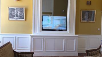Een woonkamer met een grote tv die aan een witte paneel bevestigd is, twee gestreepte banken, een gestreept tapijt en twee ingelijste foto's aan de muur.