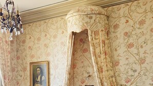 A bedroom with a four-poster bed, a chandelier, floral wallpaper, a framed picture on the wall, and a wooden floor. - Bed and breakfast at Château de Craon Swimming pool, tennis court, park Pdj included. (Craon)