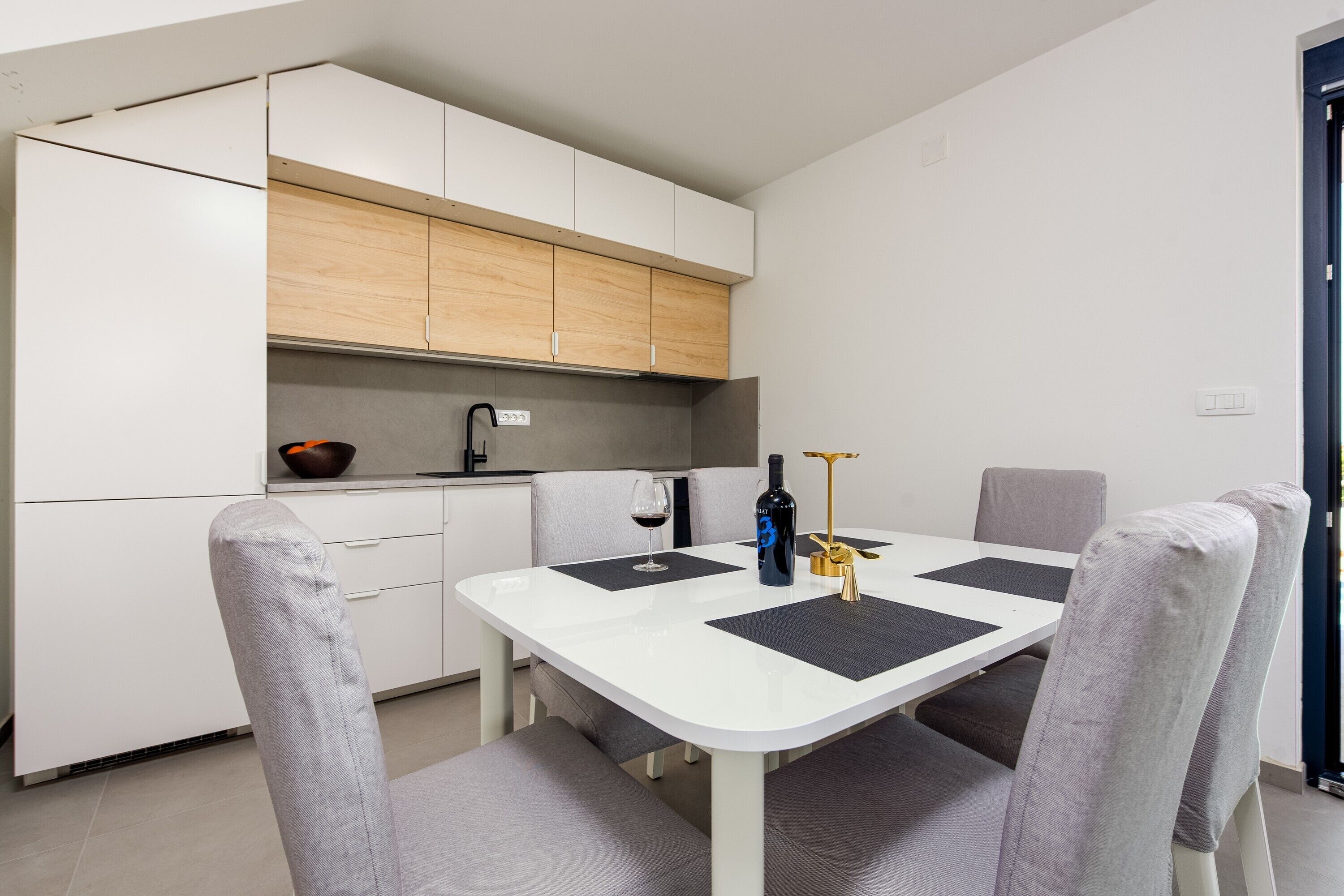 A compact kitchen with white cabinets, a dining table with four chairs, and a small countertop with a bowl and a bottle.