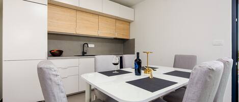 A compact kitchen with white cabinets, a dining table with four chairs, and a small countertop with a bowl and a bottle.