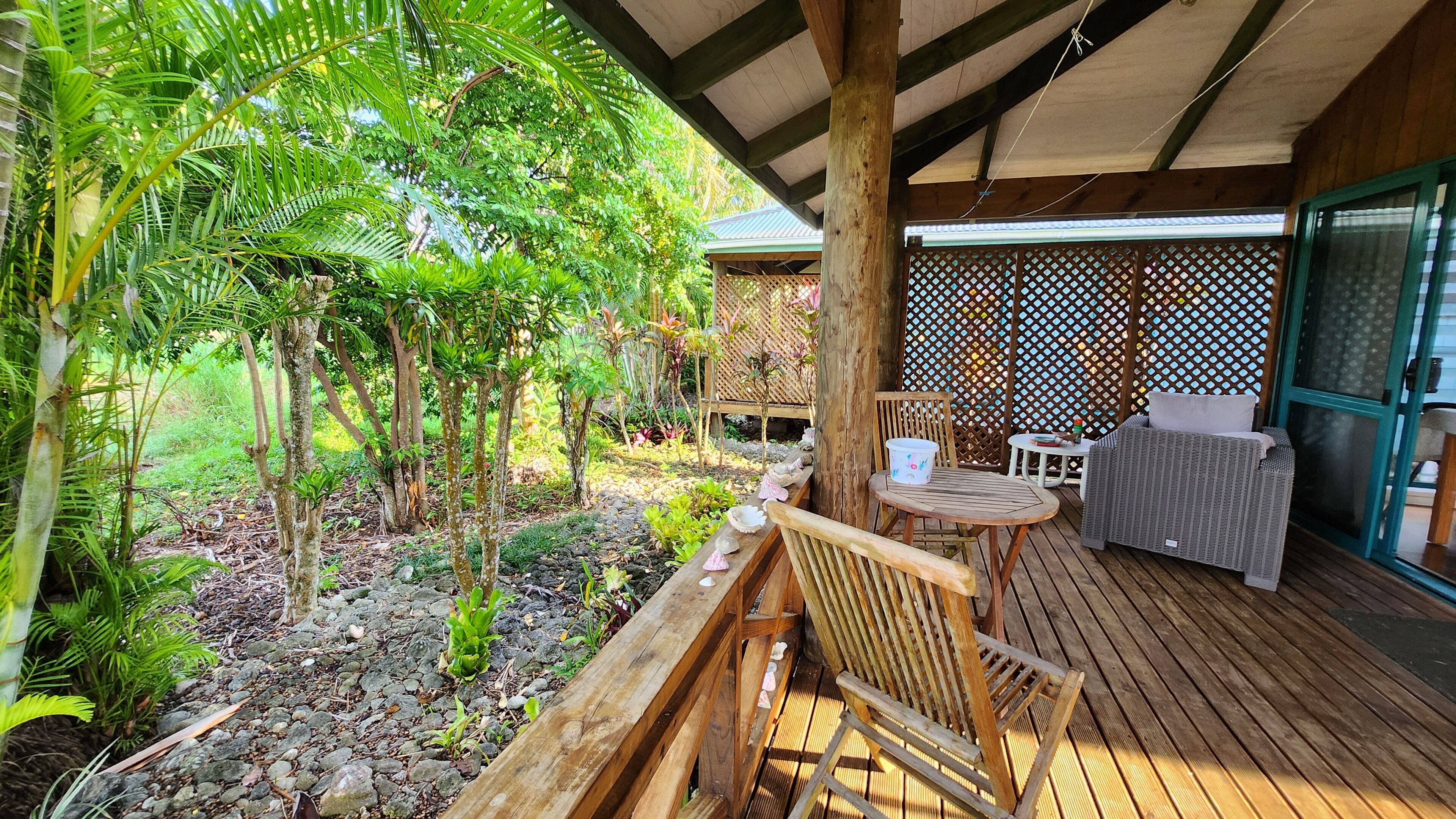 Une terrasse en bois avec une table et des chaises, entourée d’une végétation luxuriante et d’une clôture en bois.