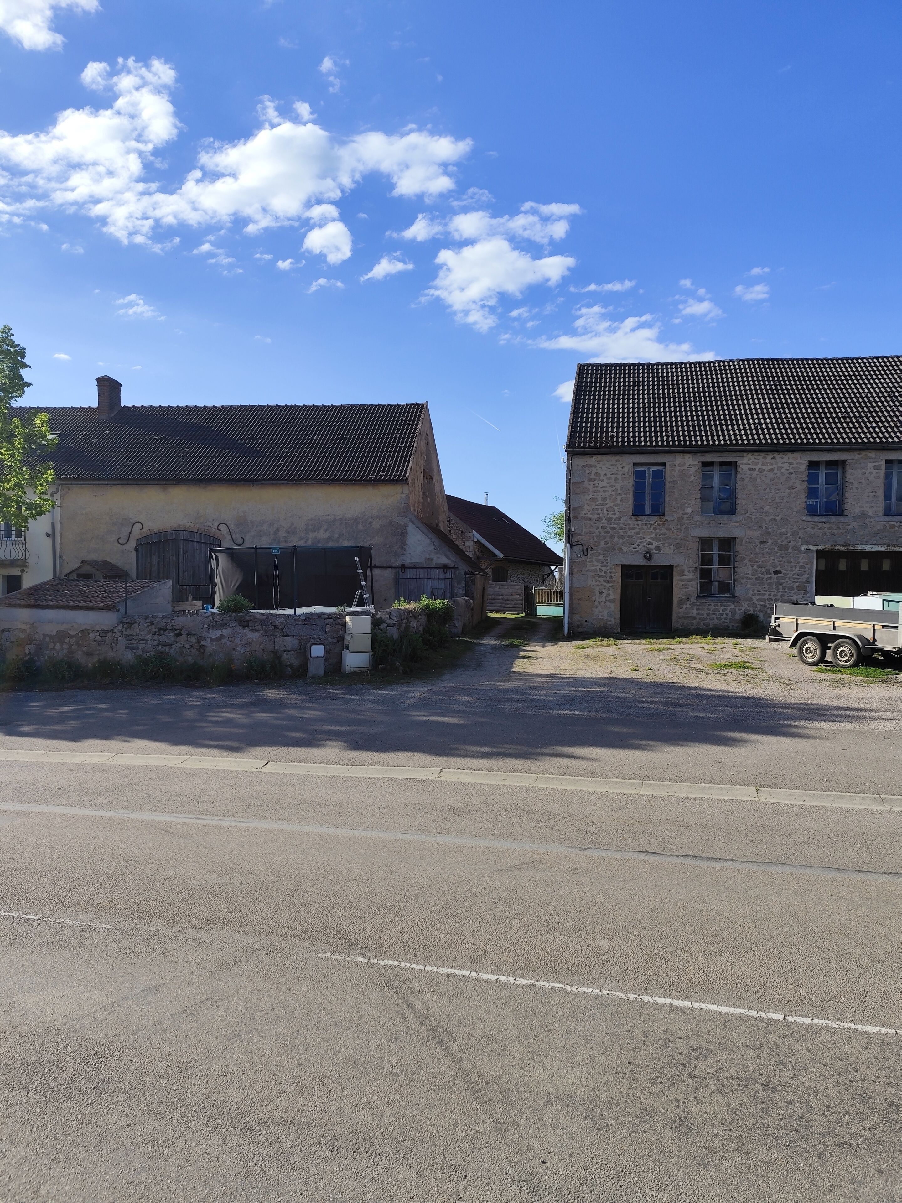 A rural street with two stone buildings, one with a tiled roof and another with a sloped roof.