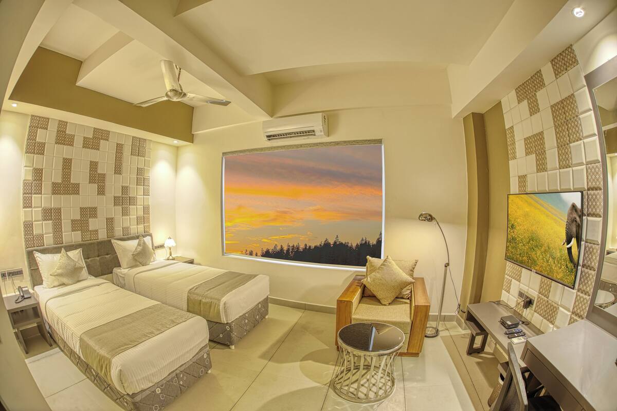 Camera d'albergo con due letti, una TV, un ventilatore a soffitto e un'ampia finestra con vista sul tramonto.