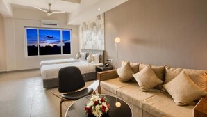 Ett modernt hotellrum med en säng, en soffa, en fåtölj, ett skrivbord och ett stort fönster med utsikt över en solnedgång.
