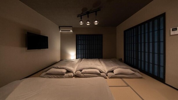 A room with a bed, a television, a ceiling light fixture, and a sliding door. - OyadoKinokuniyaSakaemachi (Nagasaki)