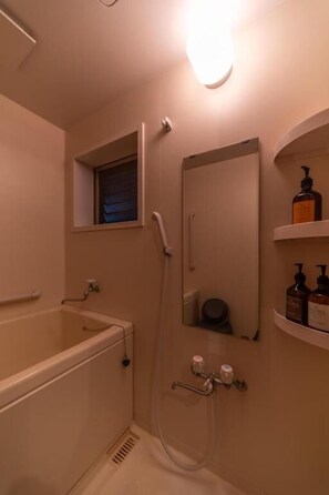 Een badkamer met een bad, douche, spiegel en een plank met toiletartikelen.