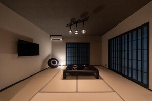 Una habitación tradicional con tatami, una mesa de tatami, un televisor montado en la pared y un puertas correderas con diseño de cuadrícula.