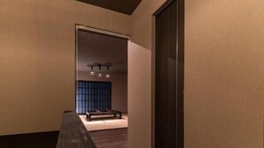 A narrow hallway with a bench, a door, and a room with a dark-colored wall and a window. - OyadoKinokuniyaSakaemachi (Nagasaki)