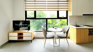 A modern kitchen with a dining area, a TV, and a window with blinds. - The LuxHomes Royal Apartment (Hai Phong)