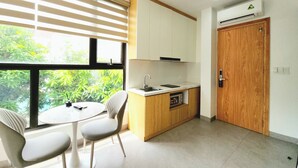 A compact kitchen with a dining area, a wooden door, and a window with blinds. - The LuxHomes Royal Apartment (Hai Phong)