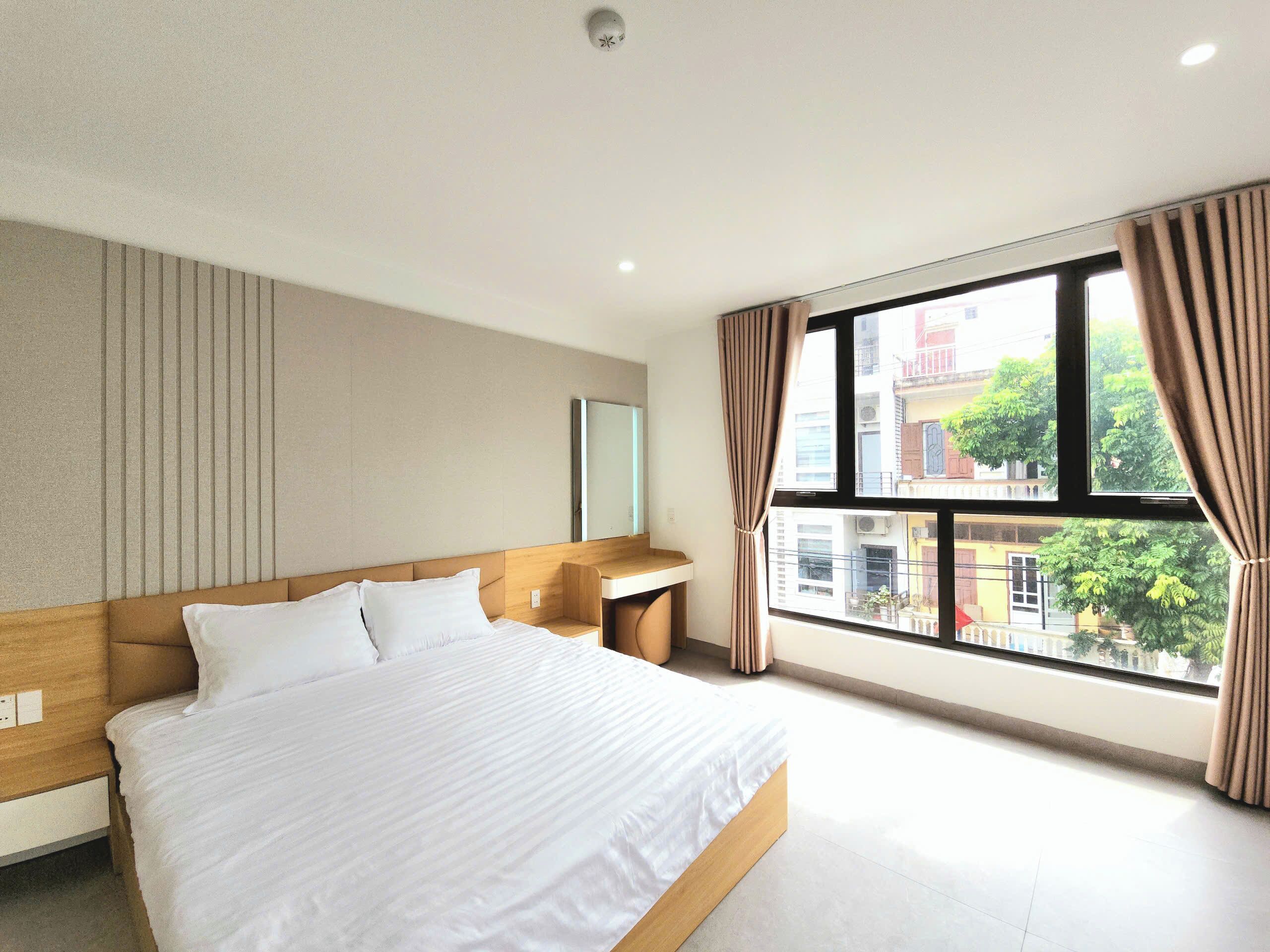 Una habitación de hotel moderna con una cama grande, una mesita de noche, un espejo y una ventana con cortinas.