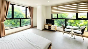 A hotel room with a bed, a desk with a TV, a chair, and large windows with curtains. - The LuxHomes Royal Apartment (Hai Phong)