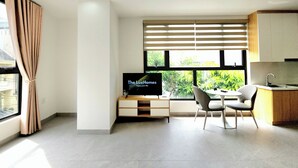 A modern living room with a flat-screen TV, a dining area with a table and chairs, and a kitchen area with a sink and cabinets. - The LuxHomes Royal Apartment (Hai Phong)