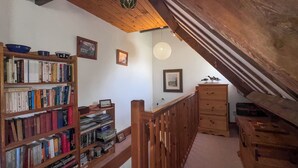 Uma escada de madeira leva a um andar superior, onde há uma estante cheia de livros e um aparador de madeira.