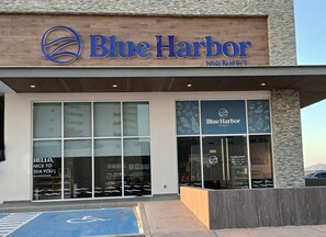 A Blue Harbor Market storefront with large windows, a wheelchair-accessible ramp, and a clear sign indicating opening hours. - Encantame Towers Soleil Resort 15thflr. Cozy brand new 1 bedroom beachside condo (Playa Encanto)