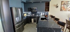 A modern kitchen with a refrigerator, microwave, and stove. There is a dining area with a table and chairs. - Encantame Towers Soleil Resort 15thflr. Cozy brand new 1 bedroom beachside condo (Playa Encanto)