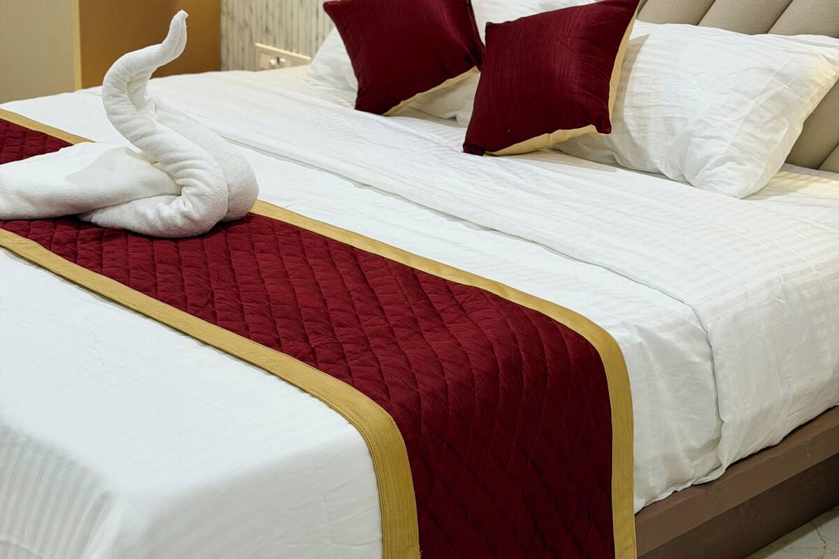 Un lit bien fait, avec une couverture rouge et dorée, une serviette blanche et deux oreillers rouges.