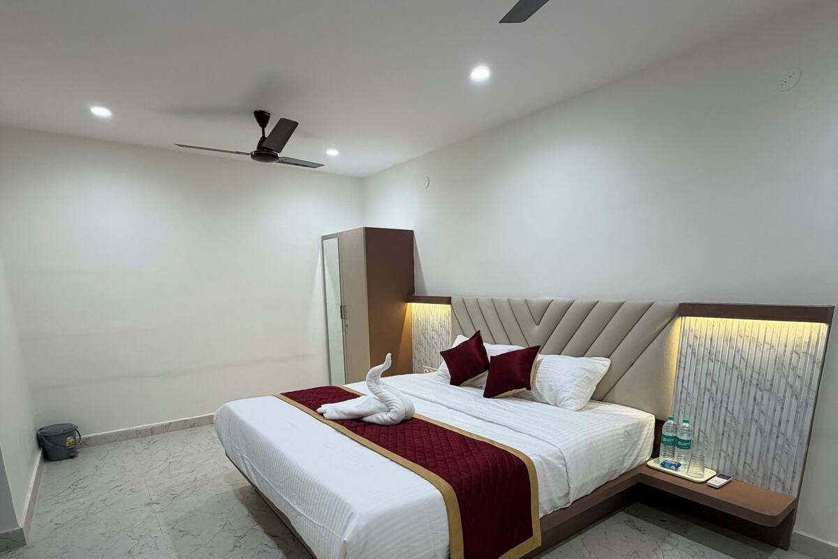 Une chambre d’hôtel équipée d’un lit, d’un ventilateur de plafond, d’une table de chevet et d’une petite table de nuit avec une lampe.