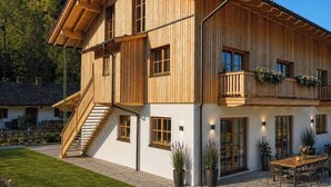 A two-story wooden house with a balcony, a staircase, and a patio area with a table and chairs. - Apartment 50sqm, balcony, kitchen, living room, bedroom, max. 2 pers. (Ruhpolding)