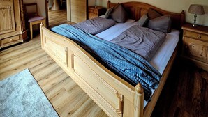 A wooden-framed bed with a blue quilt, a wooden nightstand with a lamp, and a wooden wardrobe. - Apartment 50sqm, balcony, kitchen, living room, bedroom, max. 2 pers. (Ruhpolding)
