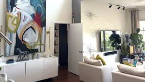 Ein geräumiges Wohnzimmer mit einem großen, abstrakten Gemälde, einer modernen Sofagarnitur, einem Flachbildfernseher und einem Essbereich mit einer Granitarbeitsplatte.