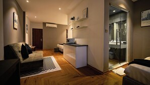 Una habitación de hotel moderna con sofá, una kitchenette pequeña, ducha de vidrio y una alfombra a cuadros.