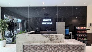 Un vestíbulo moderno con un mostrador de recepción, un amplio ventanal y un cartel que dice 'ATLANTIS APARTMENT'.