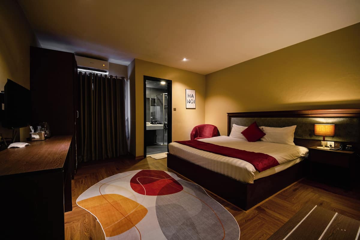 Ein Hotelzimmer mit Bett, Nachttisch, Lampe und Blick ins Badezimmer.