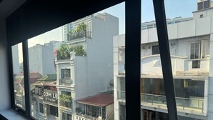 Vista a través de una ventana que muestra un edificio con balcones, un letrero con texto vietnamita y otro edificio con tejado rojo.