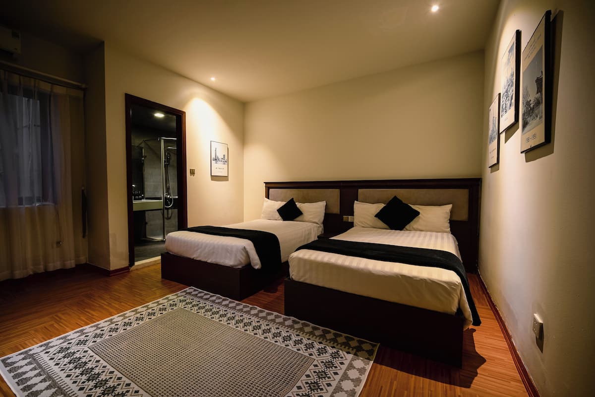 Ein Hotelzimmer mit zwei Betten, einer Duschkabine und einem gemusterten Teppich.