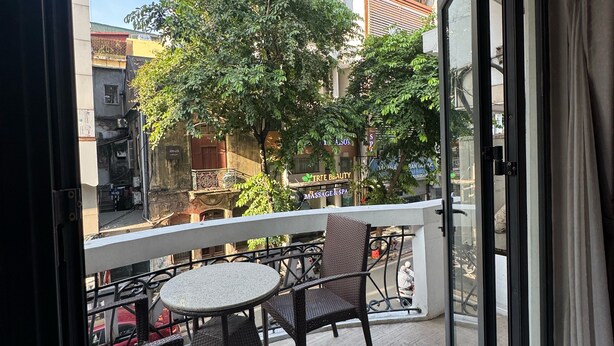 Un balcón con mesa y sillas, vista a la calle y un edificio con letrero de masajes y spa.