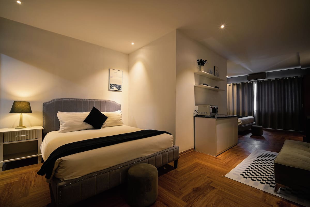 Ein modernes Hotelzimmer mit Bett, Nachttisch, Lampe und einer kleinen Küchenzeile.