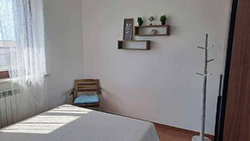 Une chambre à coucher comprenant un lit, une chaise, une étagère avec des objets décoratifs et un porte-manteau.