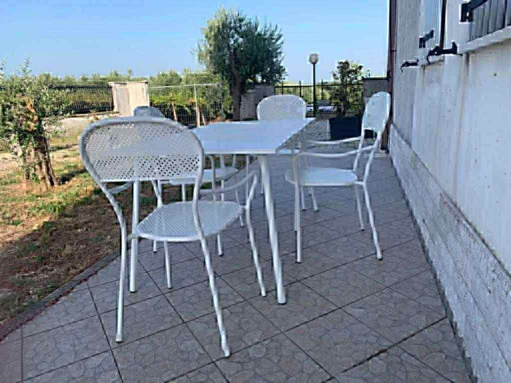 A patio with a table and four chairs, a white wall, and a fence in the background.