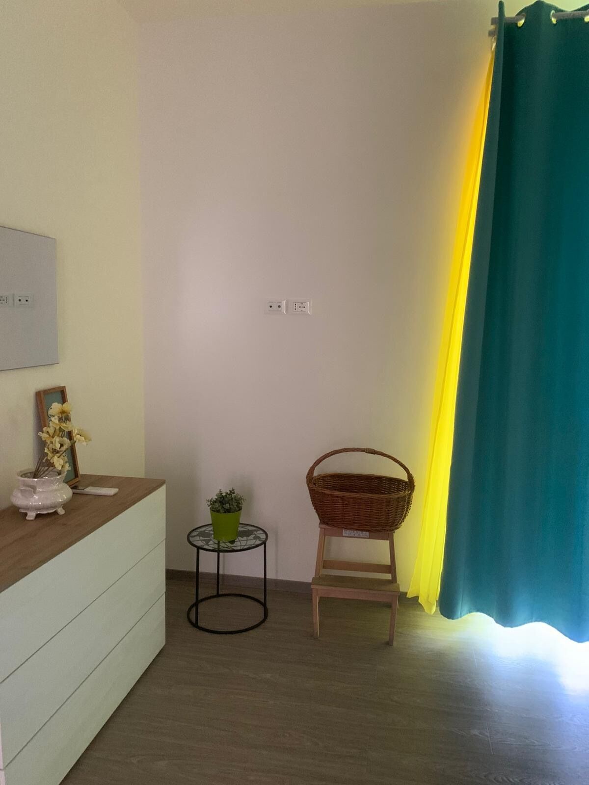 Una habitación con una encimera de madera, una mesita con una planta, una silla de mimbre y una cortina verde.