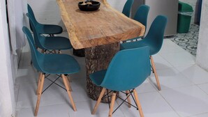 Un coin repas avec une table en bois, des chaises de couleur turquoise, un luminaire suspendu et un réfrigérateur.