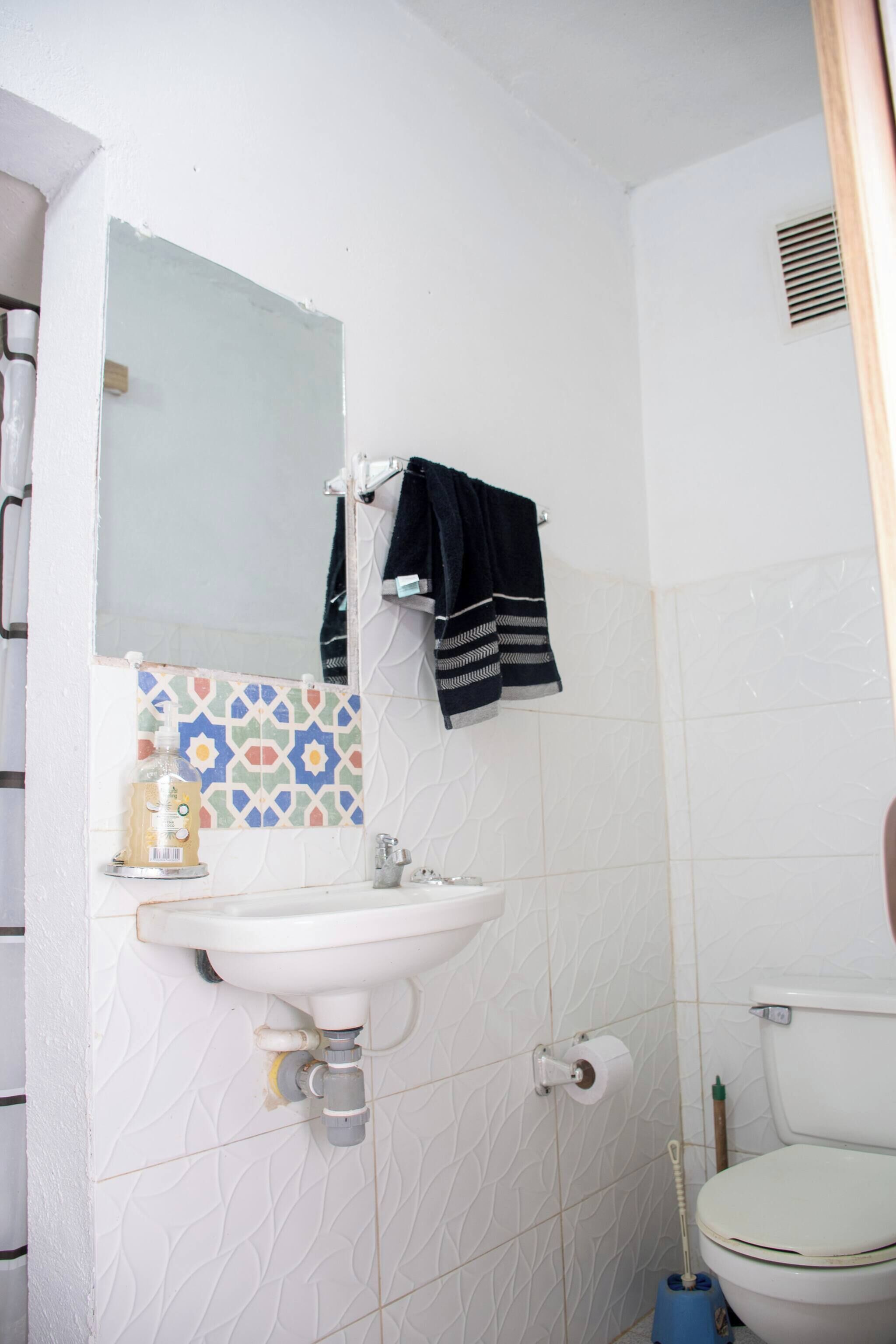 Un bagno con lavandino bianco, un water, uno specchio e una parete rivestita di piastrelle decorate.