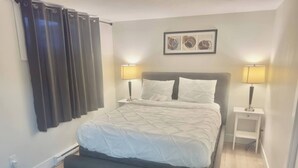 Una camera da letto con un letto, due comodini con lampade, una panca, un quadro appeso al muro e una finestra con tende.