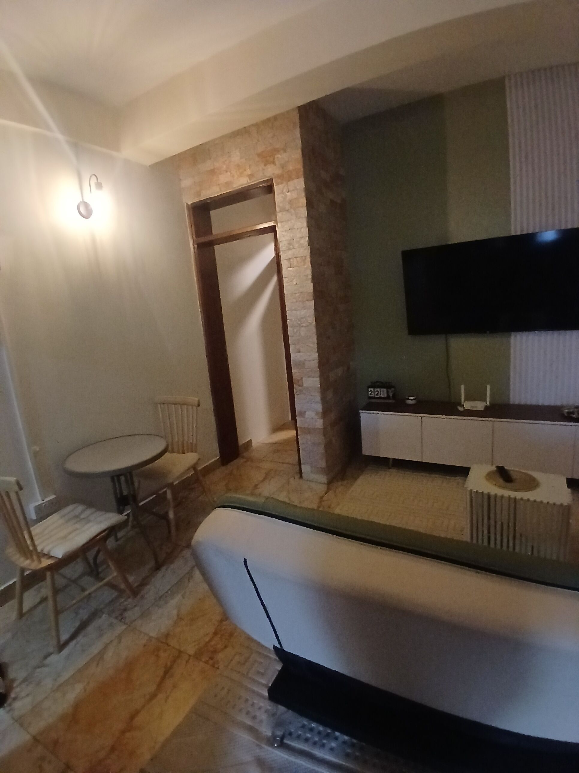 Un salon comprenant un canapé, un téléviseur, une table à manger avec des chaises et un mur décoratif en pierre.