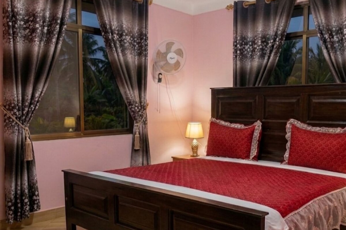 Une chambre à coucher avec un lit, des rideaux, une lampe de chevet et un ventilateur mural.