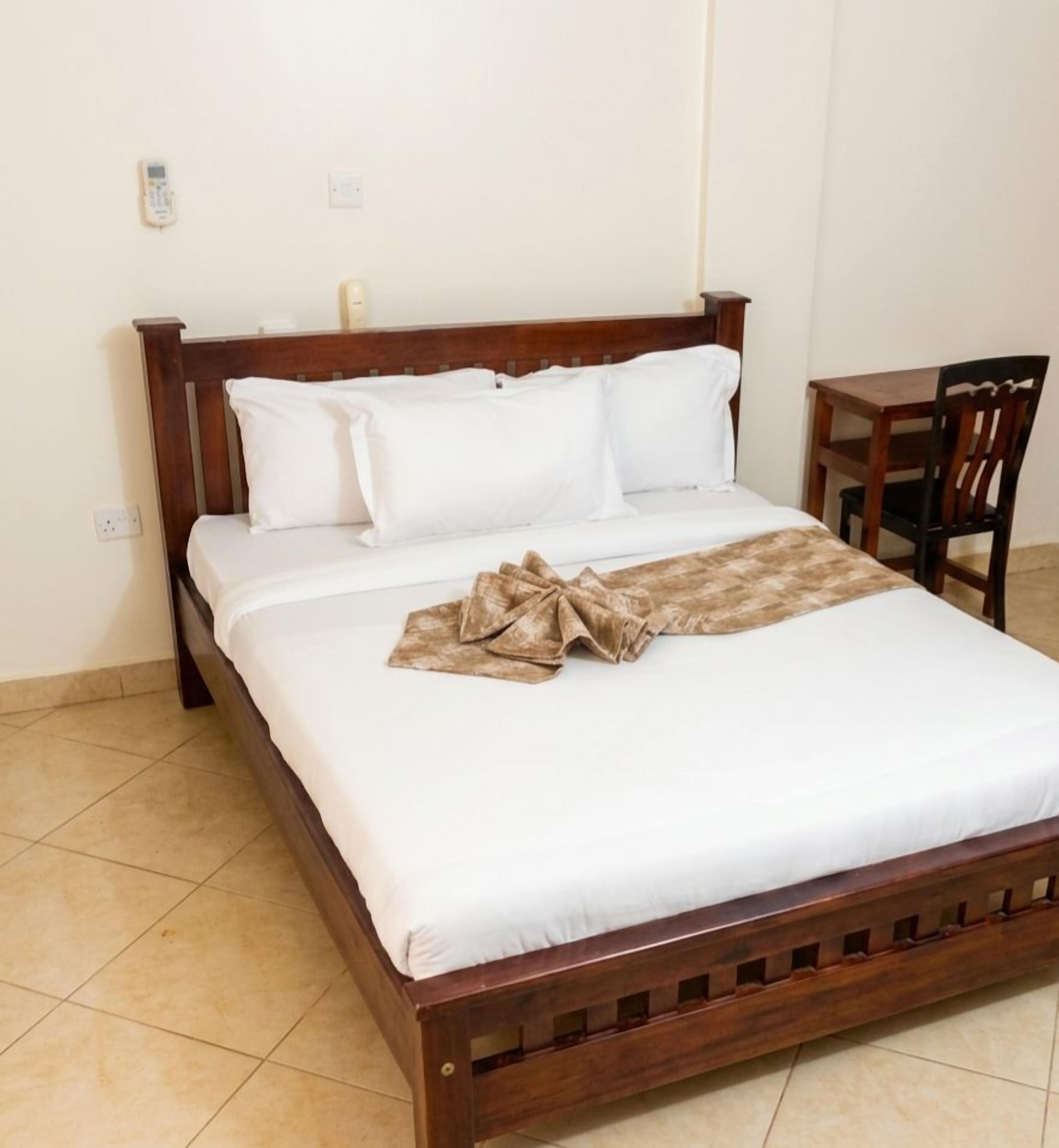 A single bed with a wooden frame, white bedding, and a brown blanket.