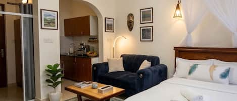 Habitación de hotel con cama, zona de estar con mesa y sillas, kitchenette y baño visible a través de un arco.
