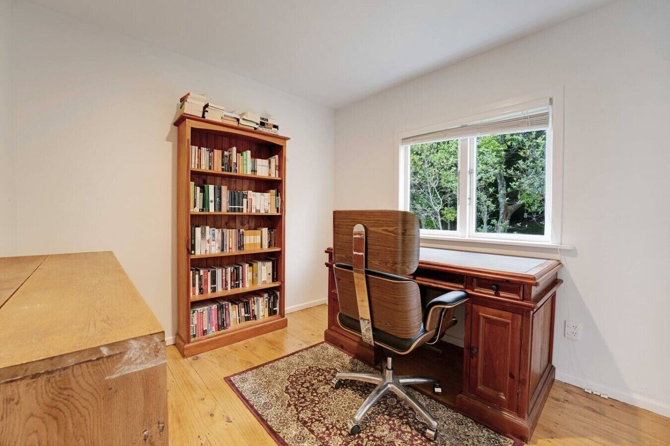 A room with a wooden desk, a chair, a bookshelf, and a window.