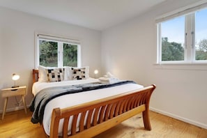 Une chambre à coucher avec un lit en bois, deux tables de chevet, une fenêtre et une vue sur la verdure.