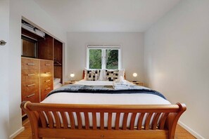 A bedroom with a wooden bed, a wardrobe, a window with a view, and bedside lamps.