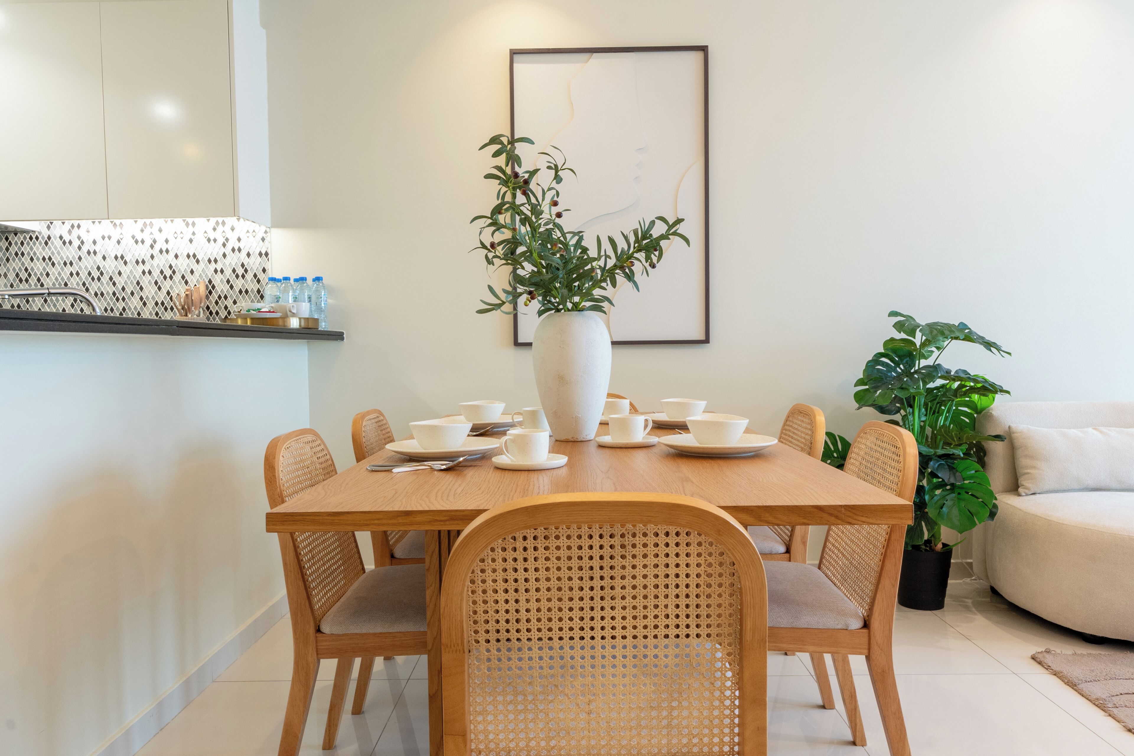 Een eethoek met een houten tafel, witte borden en bekers, omringd door rieten stoelen.