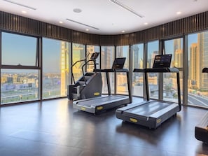 A gym with treadmills and a stair climber, large windows with a city view, and a modern interior design.