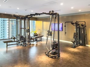 A gym with various exercise machines, a bench, and a TV screen on the wall. - Paramount Luxury 2BR-Burj Khalifa Views (Dubai)