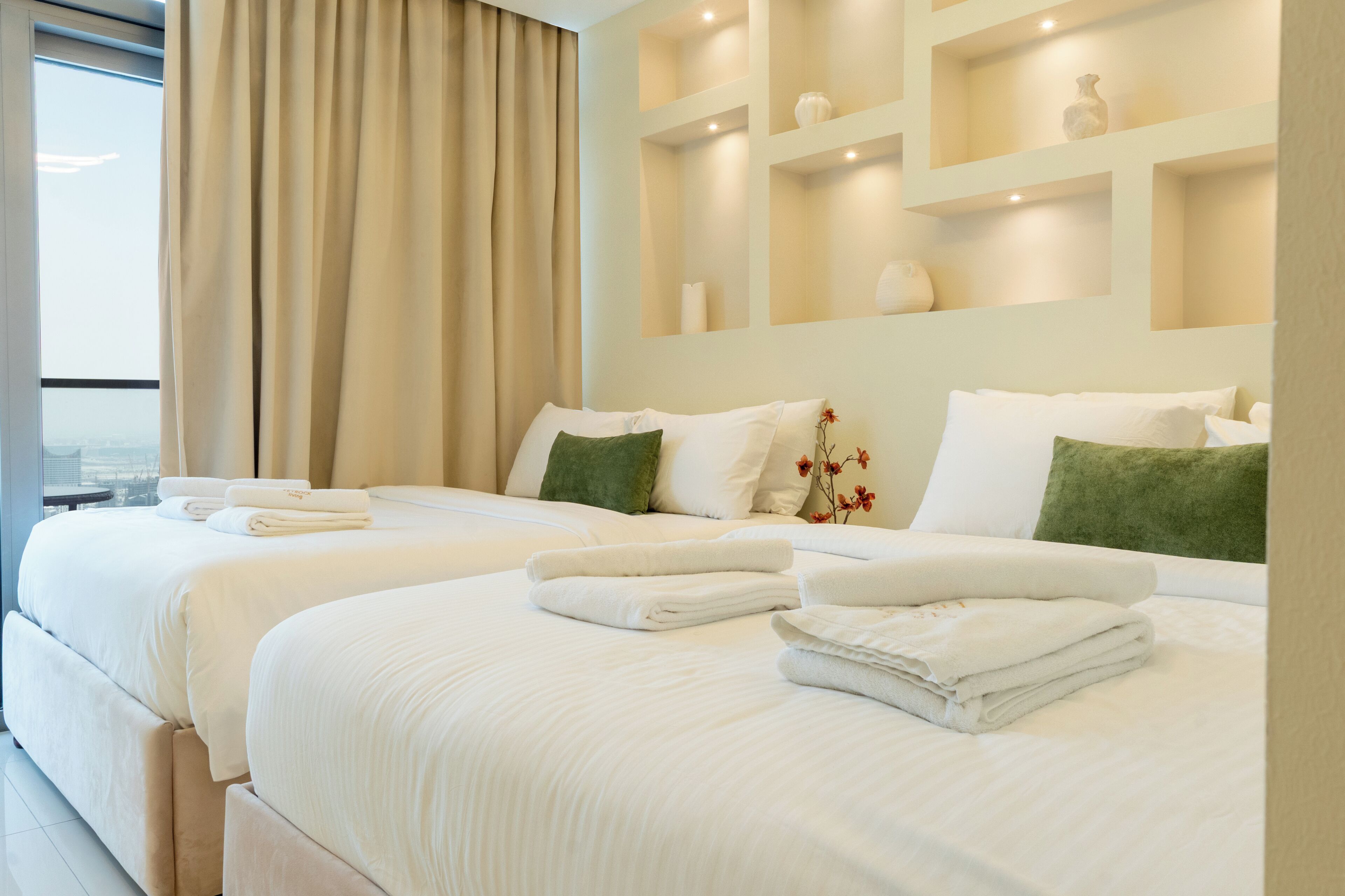 A hotel room with two beds, a large window, and a view of the city.