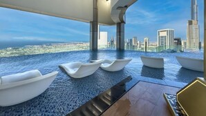 A rooftop infinity pool with white boat-shaped loungers and a view of the city skyline, including the Burj Khalifa. - Paramount Luxury 2BR-Burj Khalifa Views (Dubai)